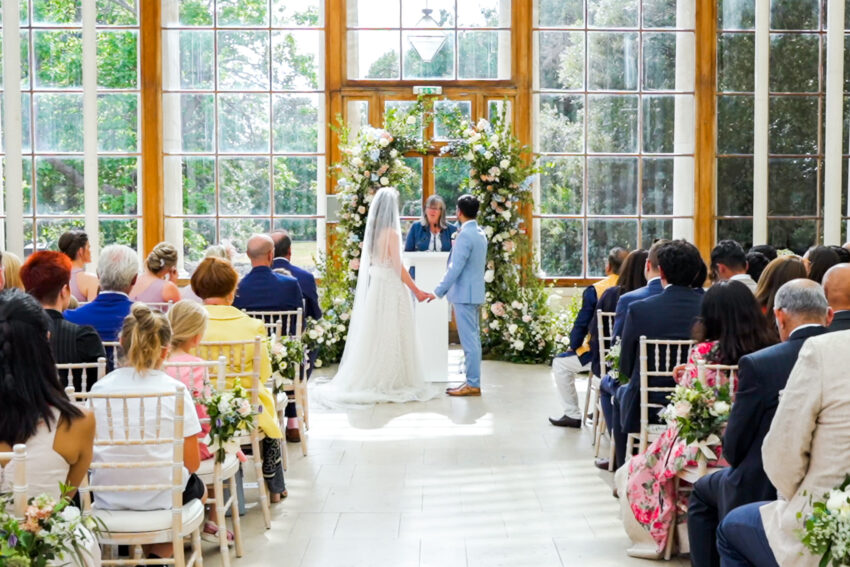 Wedding ceremony at Kew Gardens, with the bride and groom exchanging vows in a light-filled glass setting.