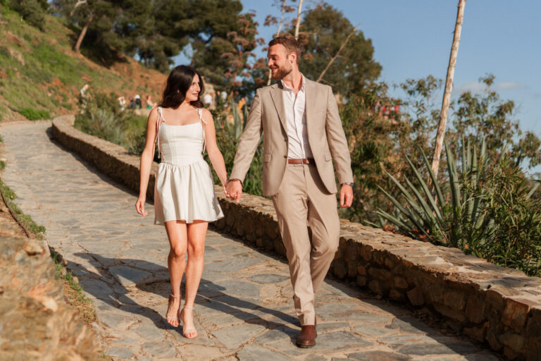 Couple walking hand in hand along a stone path during a photoshoot on Gibralfaro hill in Málaga.