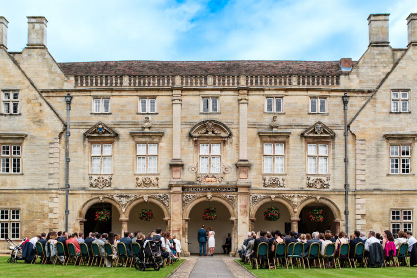 Outdoor wedding ceremony in the historic courtyard at Magdalene College Cambridge with guests seated on the lawn.