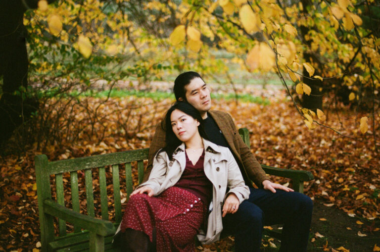 Couple sitting on a bench surrounded by autumn leaves in Cambridge Botanic Garden.