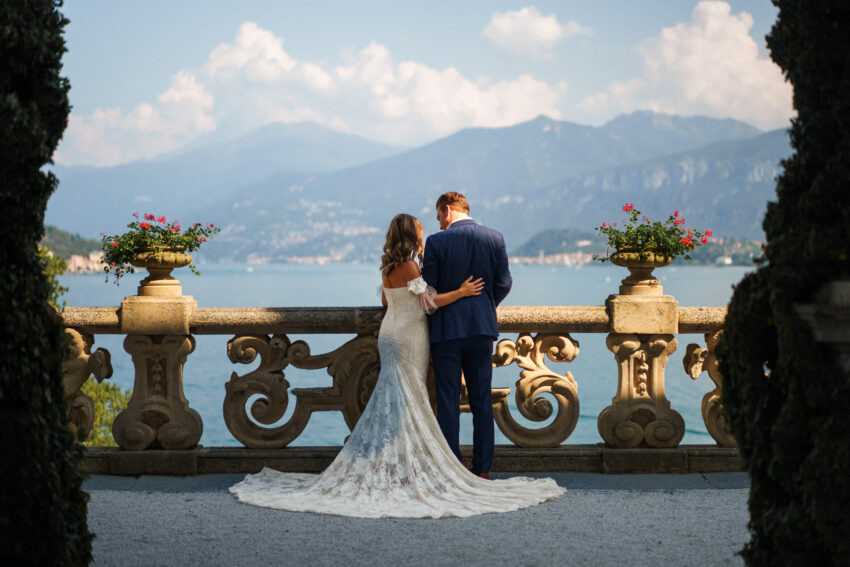 Bride and groom embracing on a lakeside terrace with sweeping mountain views, elegant composition and warm destination light.