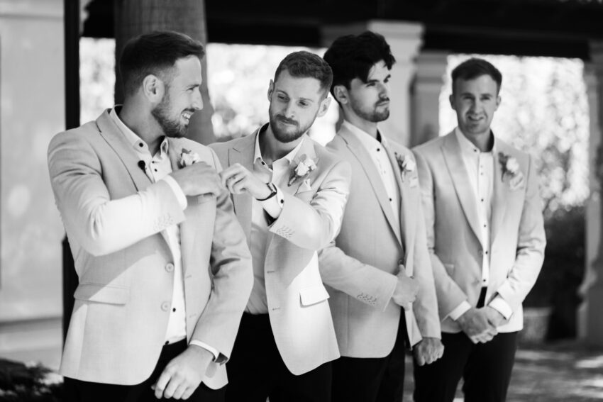 Groomsmen adjusting boutonnières in tailored suits, relaxed and natural moment captured in a refined black and white editorial wedding photograph.