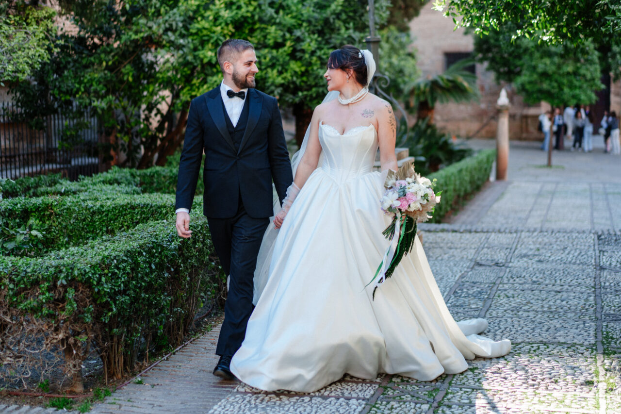 Bride and groom walking through gardens near Malaga Cathedral, natural wedding moment.
