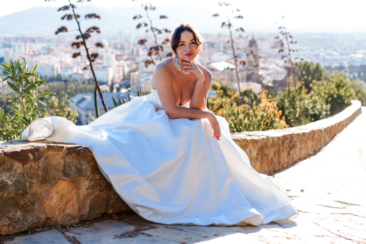 Bride sitting at Gibralfaro hill with panoramic Malaga views, soft natural light.