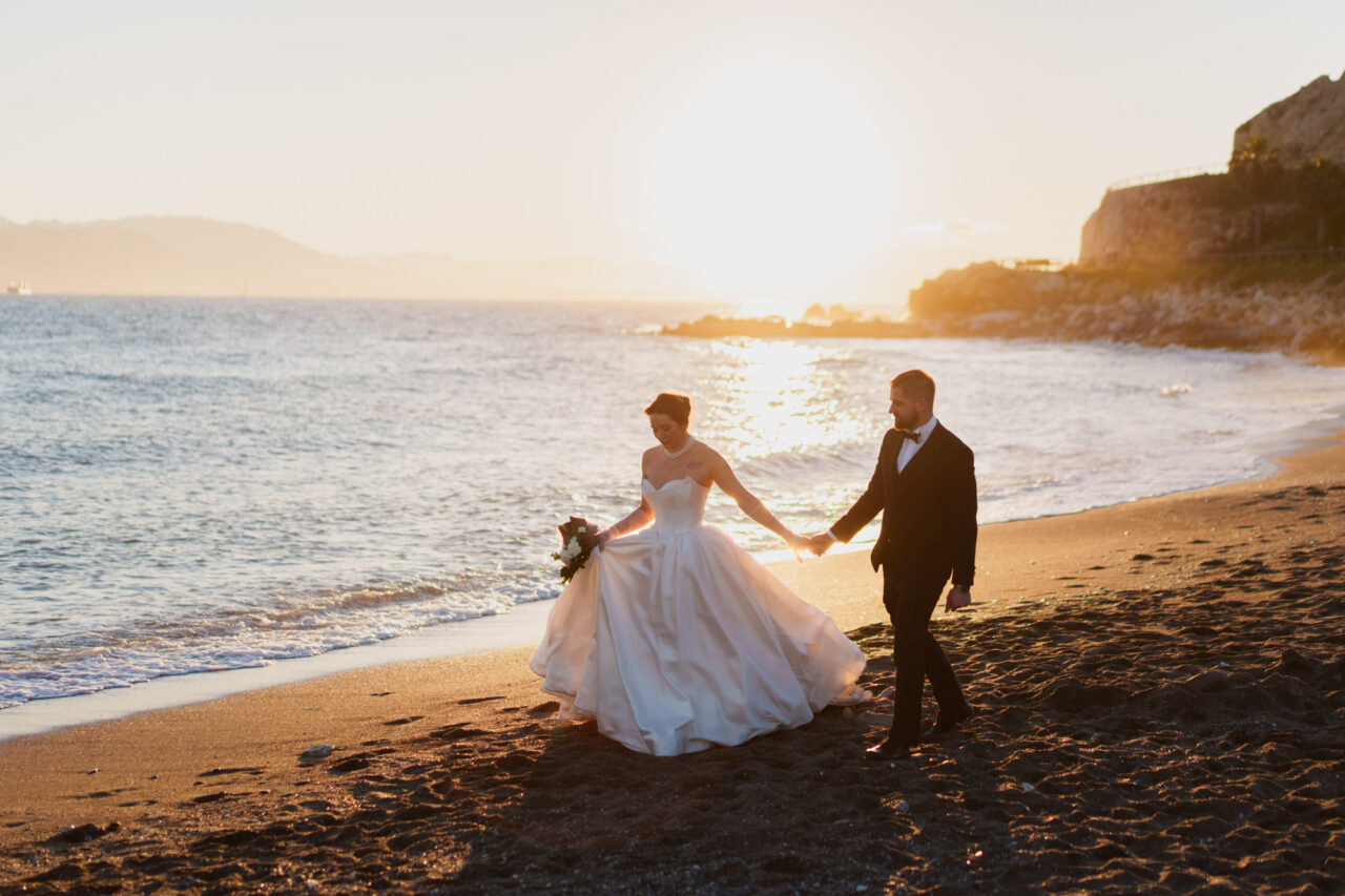 Couple walking along the Malaga coastline at sunset, relaxed beach wedding moment.