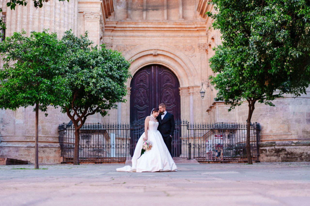 Bride and groom outside Malaga Cathedral with historic doorway in the background.