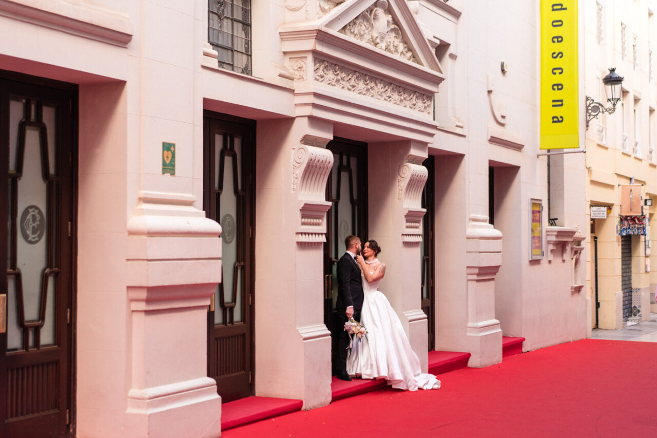 Couple outside a theatre in Malaga with pastel facade and red carpet entrance.