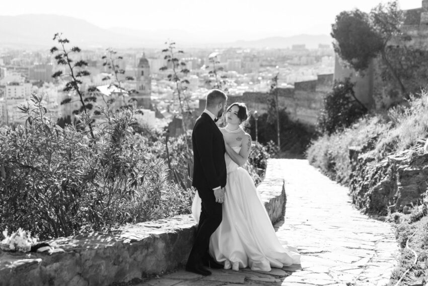 Bride and groom at Gibralfaro hill with Malaga city views, black and white wedding photo.