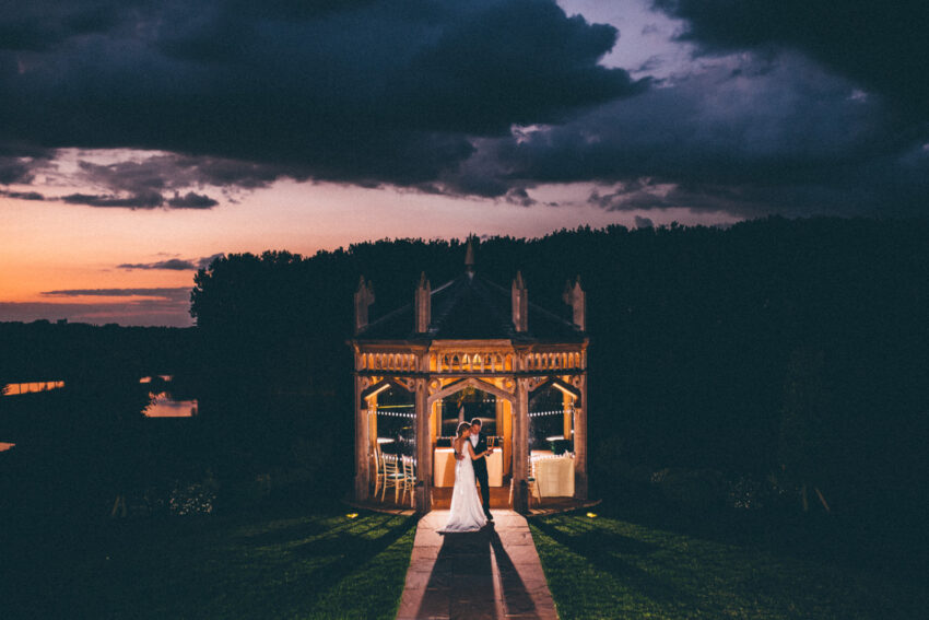 Evening portrait of the couple beneath the octagon-style ceremony structure at The Old Hall Ely wedding venue Cambridgeshire.