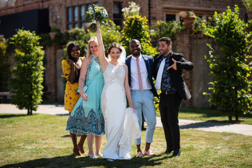 Bride celebrating with friends in the courtyard at The Old Hall Ely wedding venue Cambridgeshire.