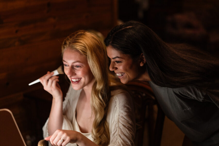Bride laughing while getting ready with her bridesmaid before the ceremony.