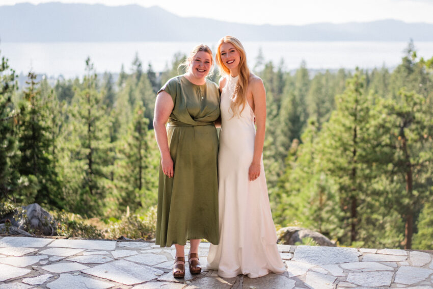 Bride posing with a bridesmaid outdoors with Lake Tahoe and forest views behind.