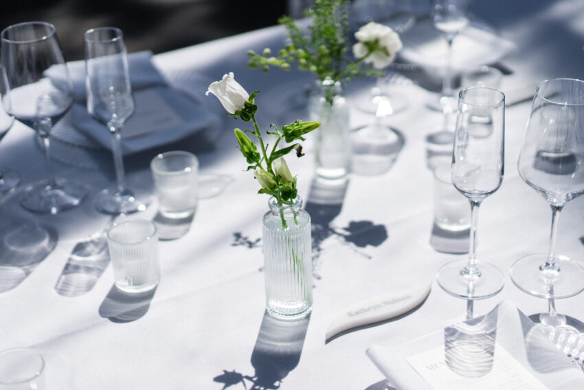 Wedding reception table with simple floral centrepieces and glassware.