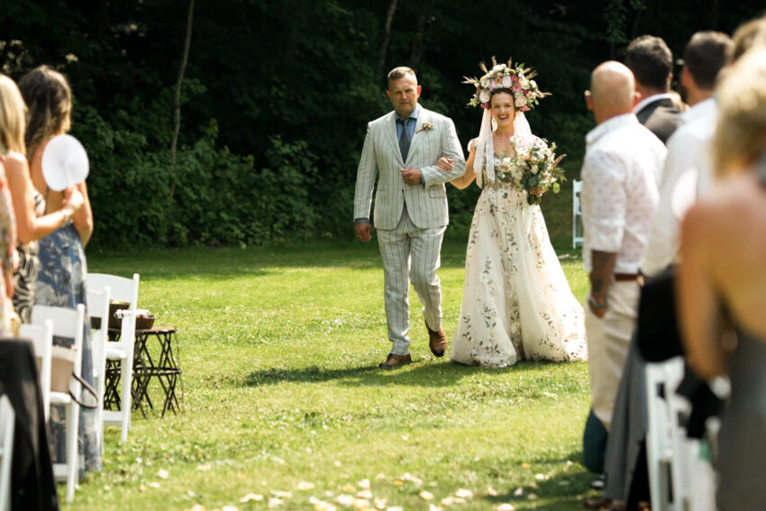 Bride walking down the aisle with her father during a lakeside wedding ceremony at Trillium Resort & Spa.