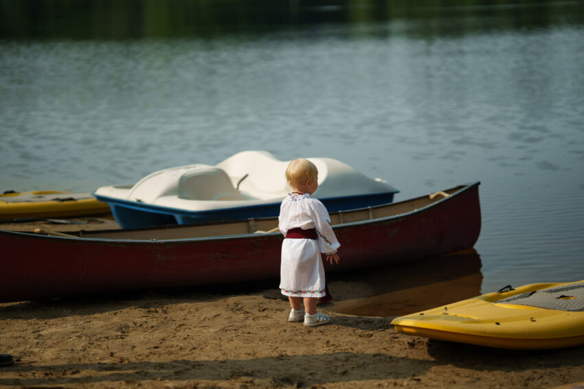 Small child standing beside canoes and paddle boats on the lakeshore at Trillium Resort & Spa.