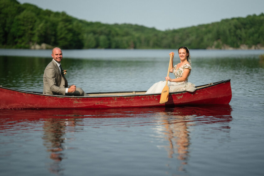 Bride and groom paddling a red canoe on the lake during portraits at Trillium Resort & Spa in Muskoka.