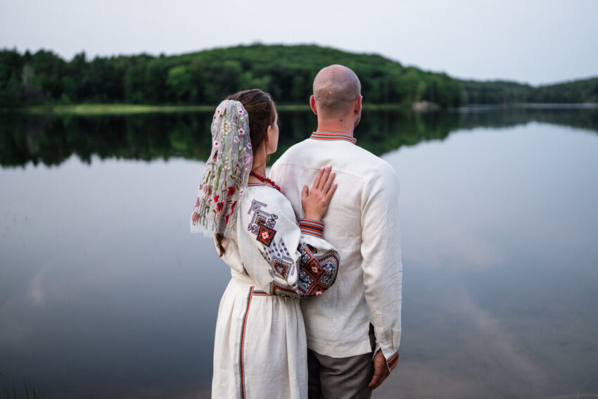 Bride resting her hand on the groom’s back as they look across the lake at Trillium Resort & Spa in Muskoka, Ontario.