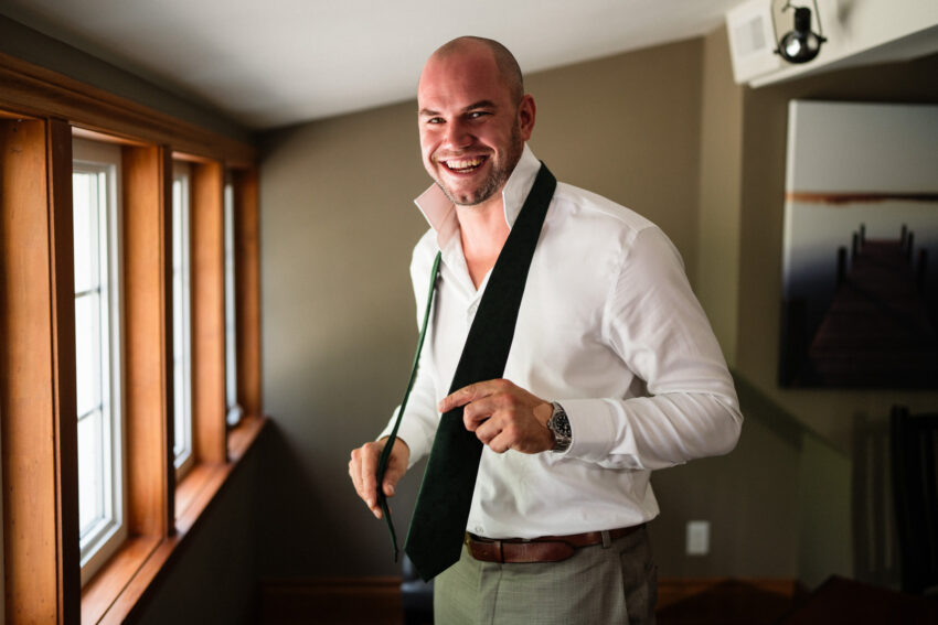 Groom smiling while putting on his tie during wedding preparations at Trillium Resort & Spa.