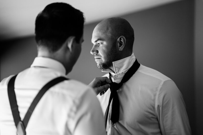 Groom adjusting his tie with help from a groomsman before the wedding at Trillium Resort & Spa in Muskoka.
