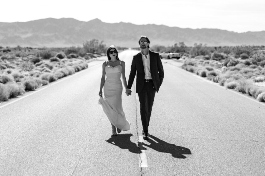 Couple walking hand in hand down an empty desert road after their ceremony, captured in a relaxed, editorial style by a Las Vegas elopement photographer.
