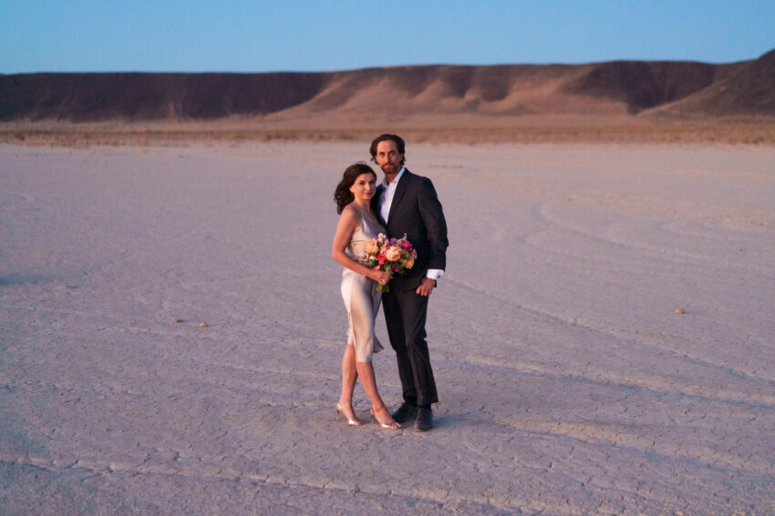 Newly married couple standing together on a vast desert landscape at golden hour with soft pastel light, photographed by a Las Vegas elopement photographer.