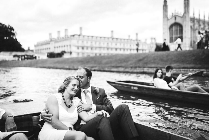 Black and white 35mm analogue wedding photograph of a bride and groom embracing in a punt on the River Cam in Cambridge, with King’s College Chapel softly blurred in the background.