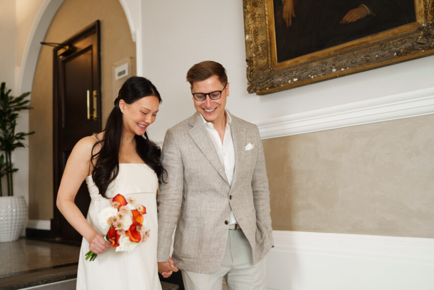 Bride and groom descend the grand staircase at Chelsea Old Town Hall, sharing a quiet smile as they make their way towards the ceremony together.