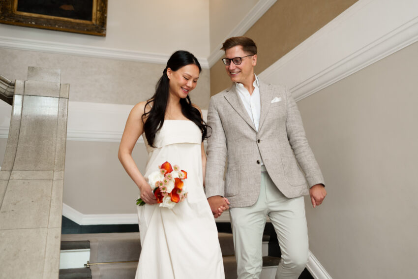Bride and groom holding hands and smiling as they walk through the elegant corridors of Chelsea Old Town Hall moments before their wedding ceremony.