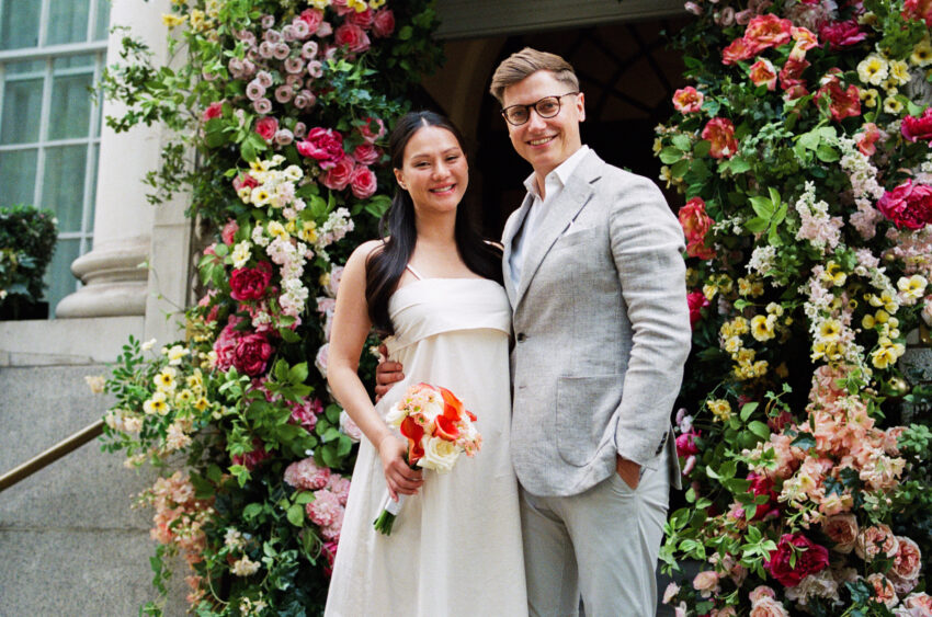 Bride and groom smiling together outside Chelsea Old Town Hall in front of the iconic flower-covered entrance following their wedding ceremony.