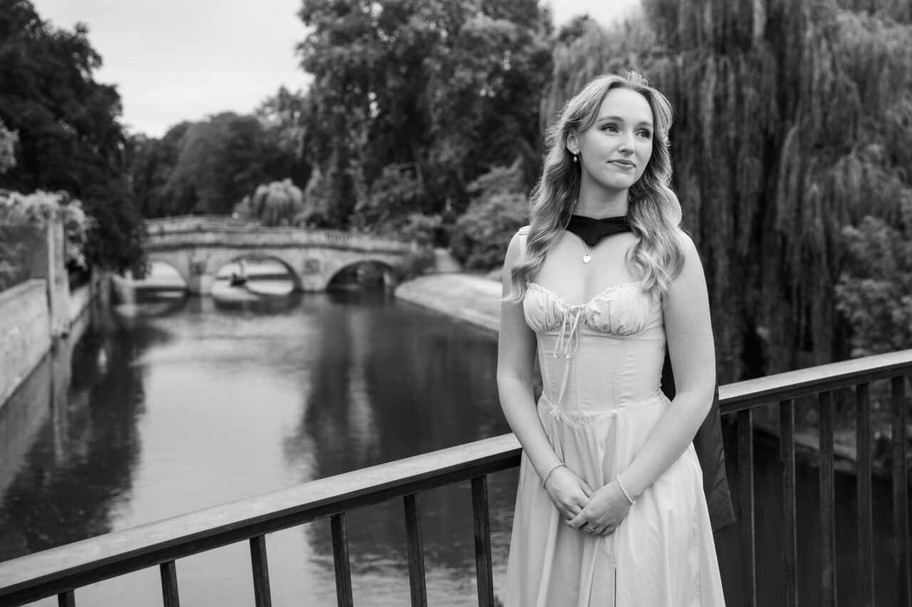 Graduate in graduation gown on Garret Hostel Bridge with Clare Bridge and punting on the River Cam, Cambridge