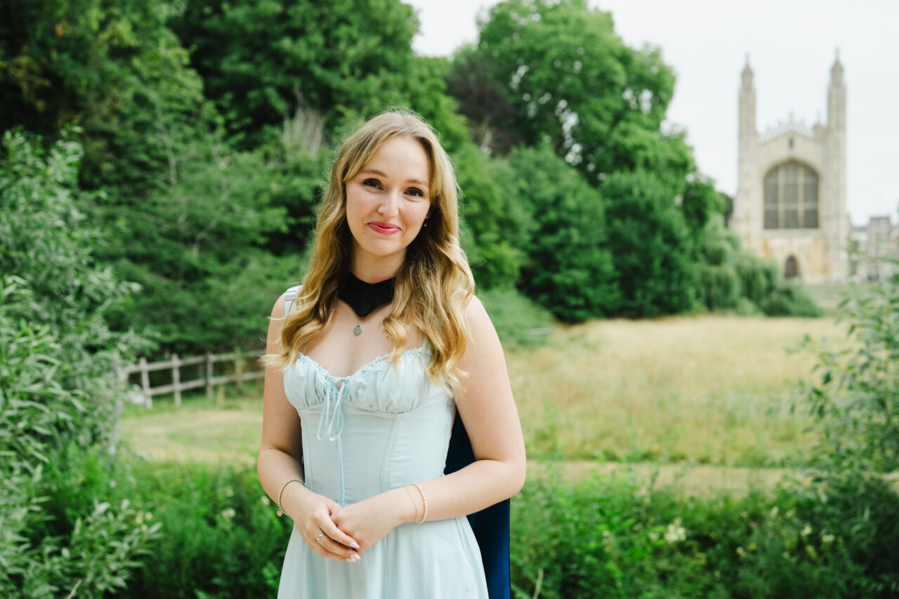 Graduation photo of Cambridge graduate in gown with King's College Chapel in the background at The Backs
