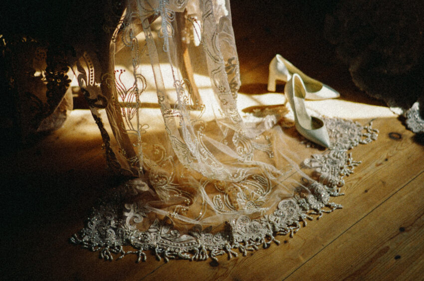 Warm, grainy film photograph of intricate bridal dress embroidery and elegant wedding shoes at a wedding in Norway.