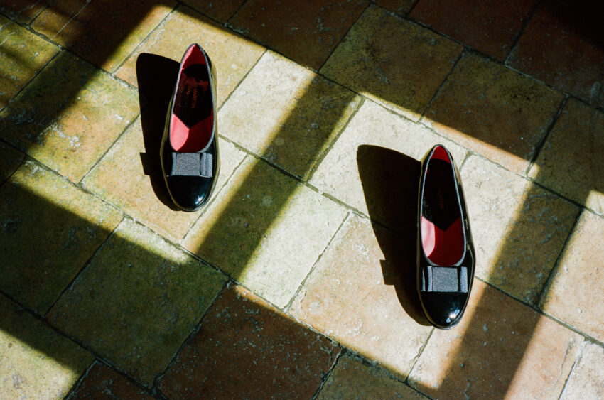 Black patent leather groom's shoes with red interiors on sunlit terracotta tiles at a wedding near Barcelona.