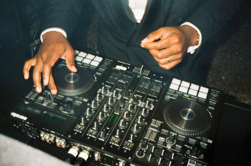 A groom mixing music on DJ decks at his wedding reception, captured on grainy 35mm film.