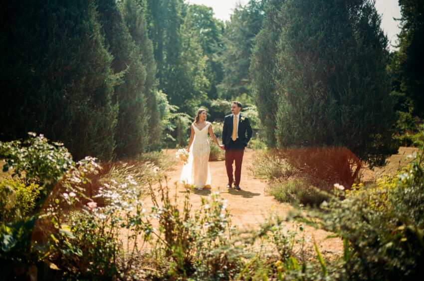 Couple walking hand in hand through a sunlit garden, photographed on 35mm film with warm lens flare.