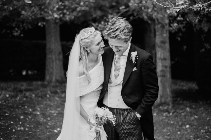 Intimate black and white wedding portrait of a bride and groom smiling together beneath the trees.