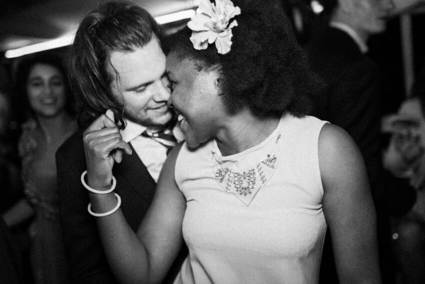 Two wedding guests dancing and laughing together in a close-up black and white photograph at a lively wedding reception.